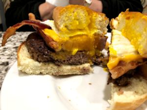 Cross section of burger with ham steak, bacon, and fried egg