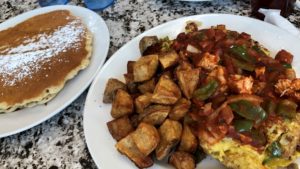 Gant omelet covered in chicken and andouille jambalaya with a side of American fries and two huge pancakes on a separate plate
